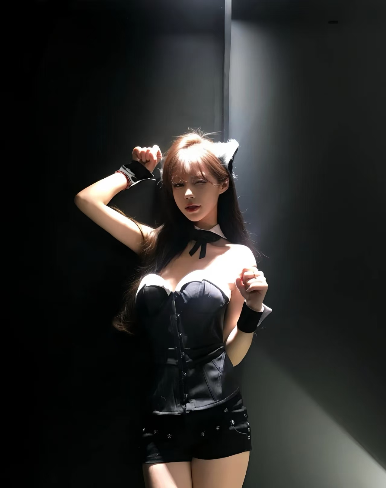 Young woman posing under a spotlight in a dark room wearing a black corset outfit and cat-ear accessories — Nunawading Brothel