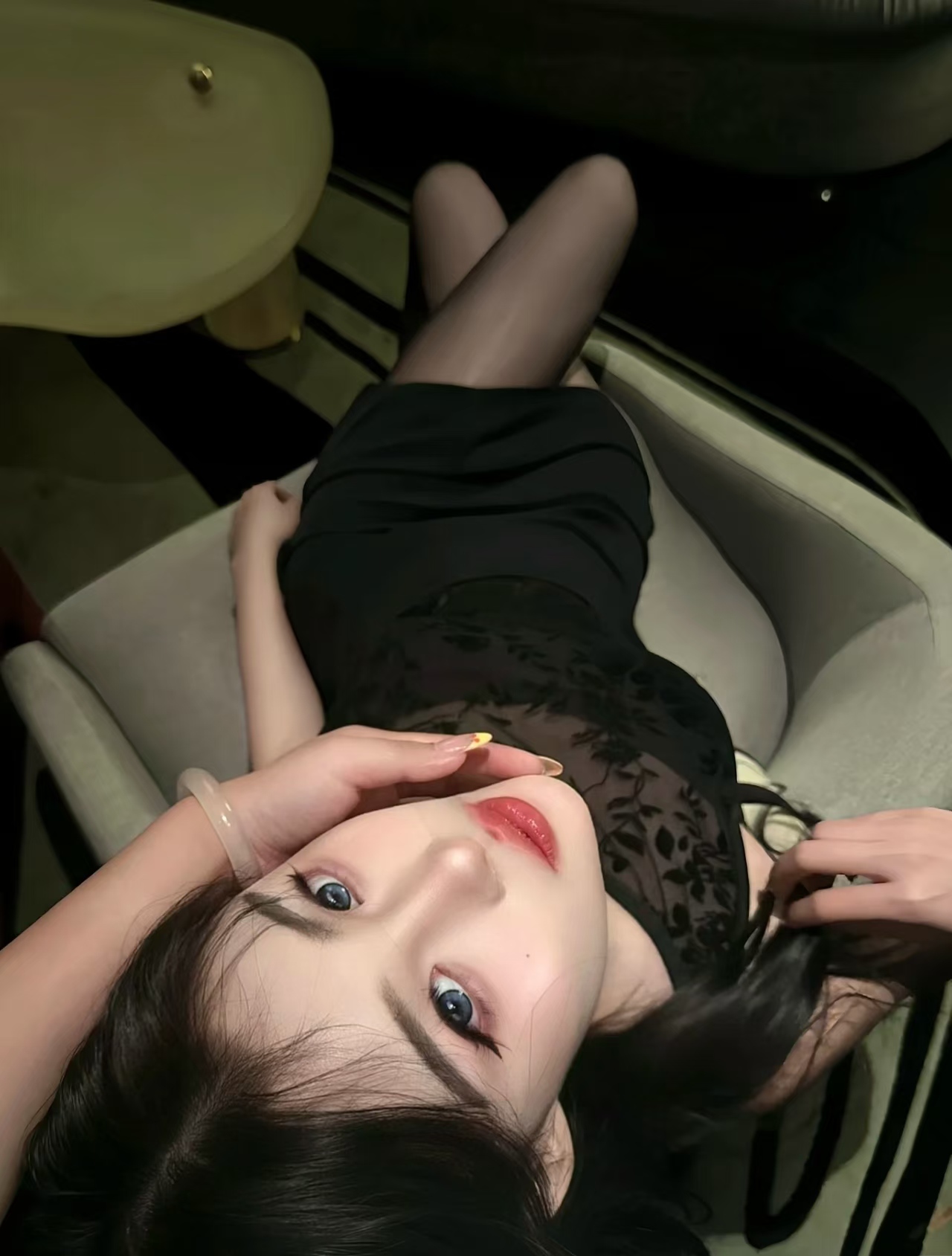 Woman in black dress and sheer stockings lying on a chair with soft lighting